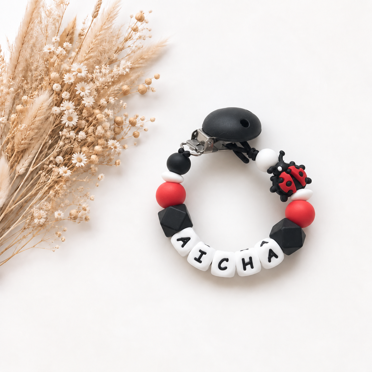 Speenkoord met naam Aicha in rood zwart en wit met een lieveheersbeestje