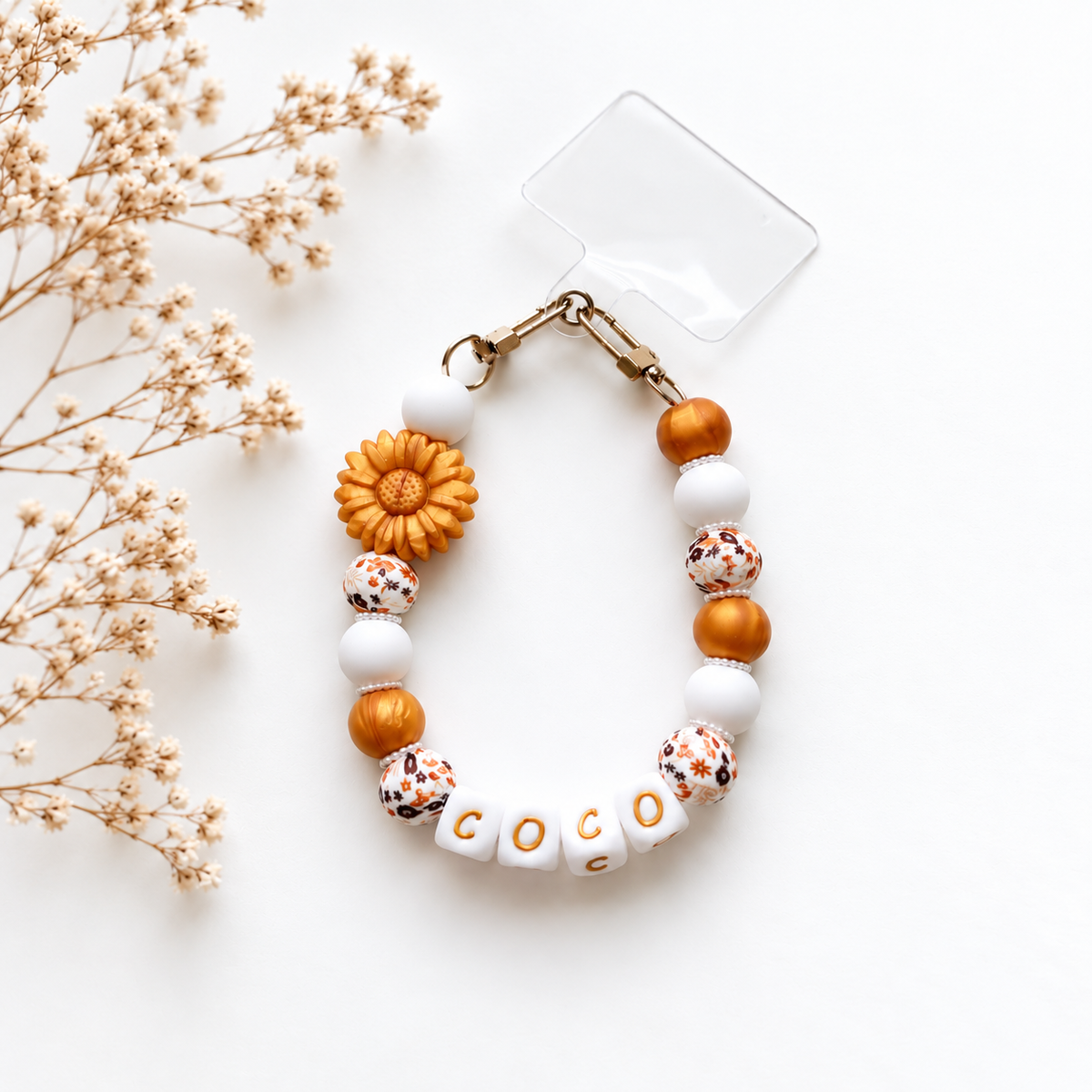Golden Bloom 3-in-1 accessoire met naam, amberkleurige en witte kralen, bloemenprints, een zonnebloem en goudkleurige bevestiging.