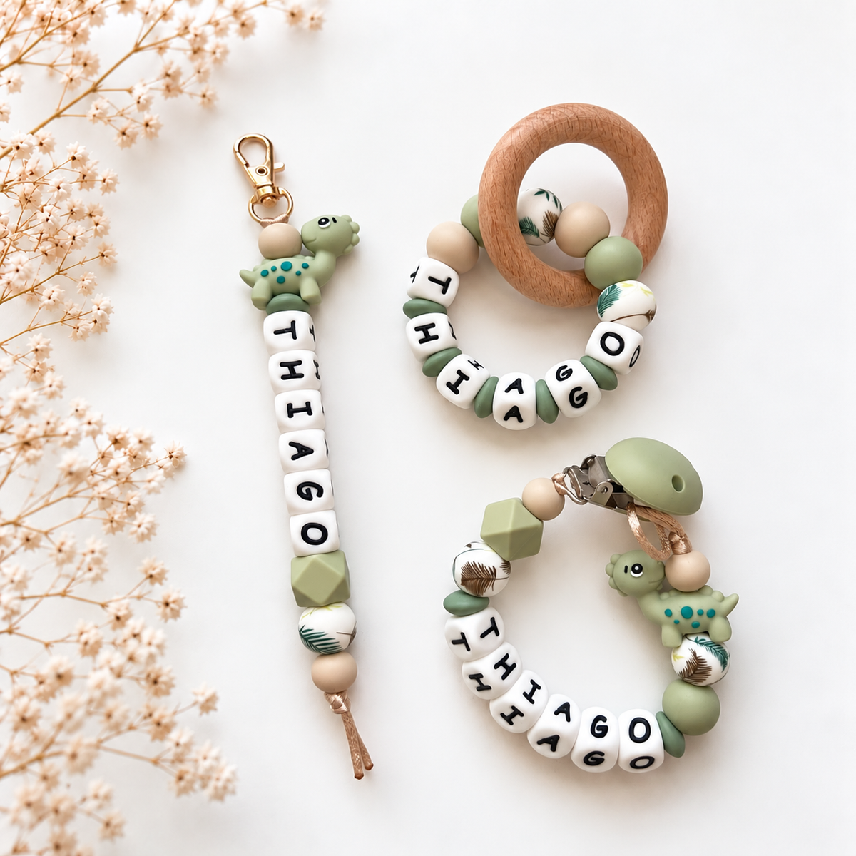 Kraamcadeauset Little Dino met speenkoord met naam Thiago, bijpassende sleutelhanger en houten bijtring in groen en beige met dinosaurusdetails.