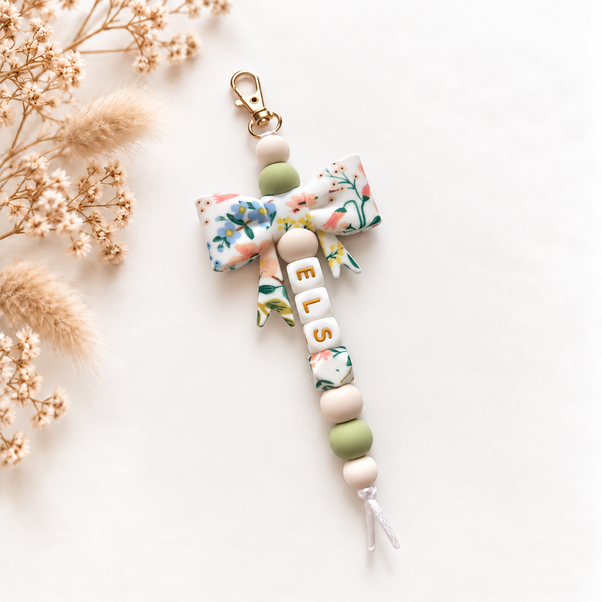 Handgemaakte sleutelhanger met naam Elise, grote bloemenstrik in groen en wit en goudkleurige letters