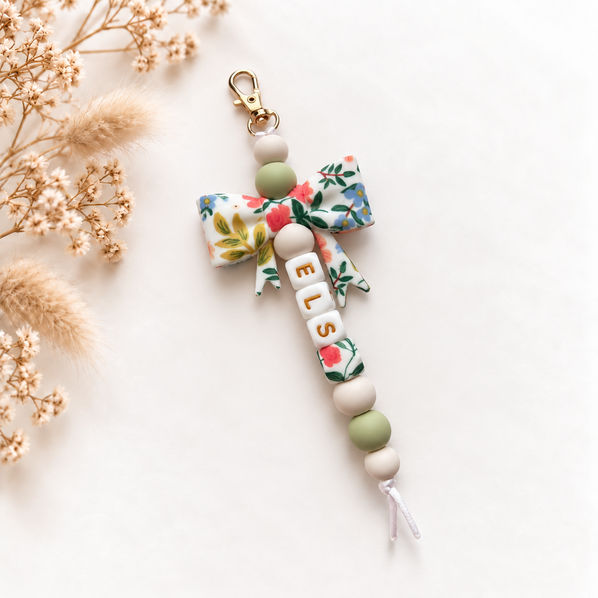 Handgemaakte sleutelhanger met naam Elise, grote bloemenstrik in groen en wit en goudkleurige letters
